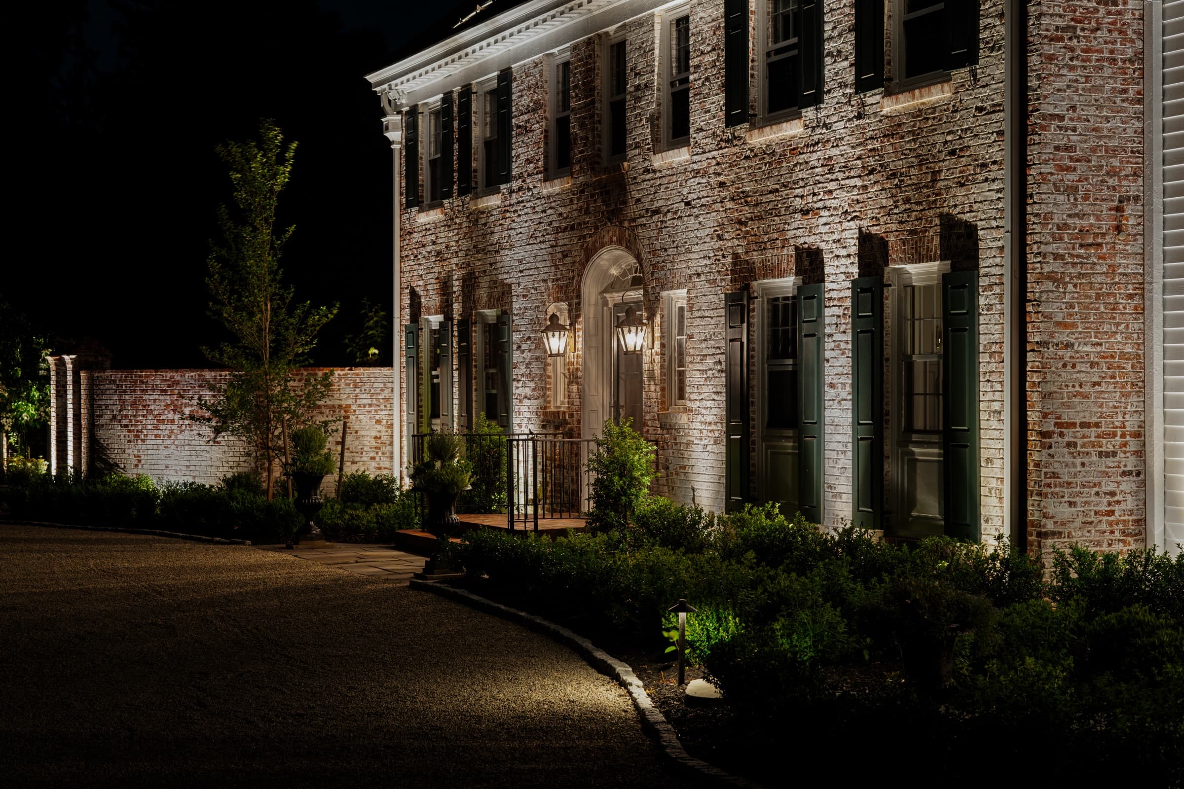 Planting beds and clipped hedging lit along the front of the house