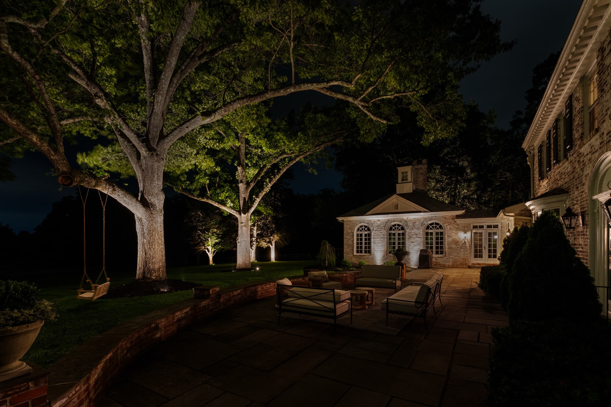 Garden beds and lawn edge lit low, house lights beyond