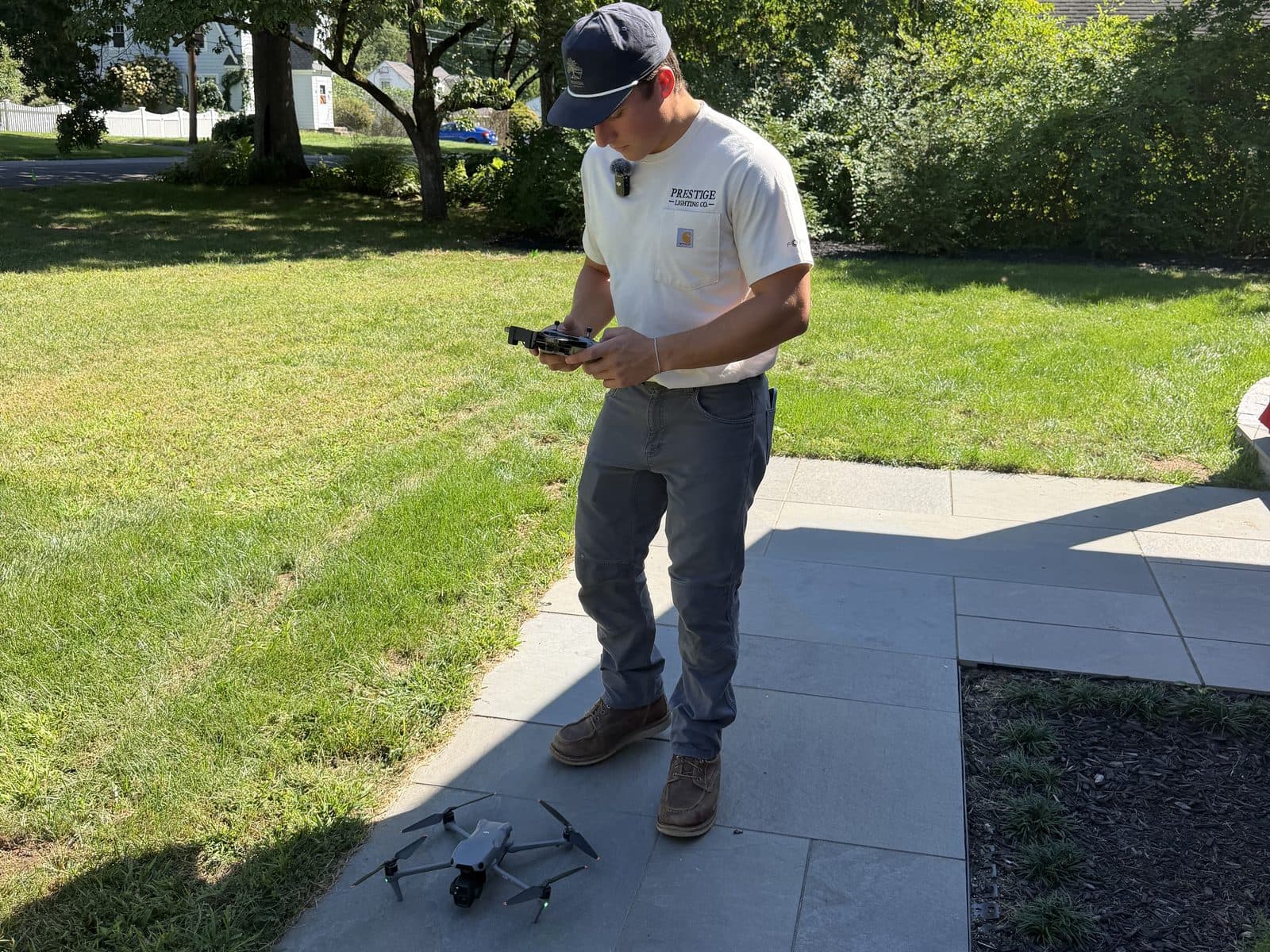 Checking a drone controller on a front walkway, the drone on the ground beside him